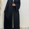 Eine Frau trägt eine lange, schwarze, fließende Abaya-Kaftan mit offenem Front und weißem Hijab.
