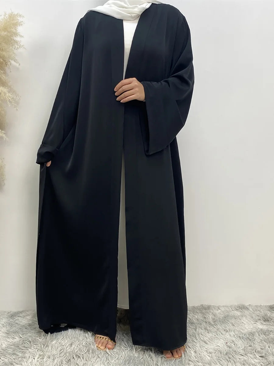 Eine Frau trägt eine lange, schwarze, fließende Abaya-Kaftan mit offenem Front und weißem Hijab.