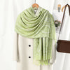 Un chal de bordado paisley vintage verde claro colgado sobre un percha beige.