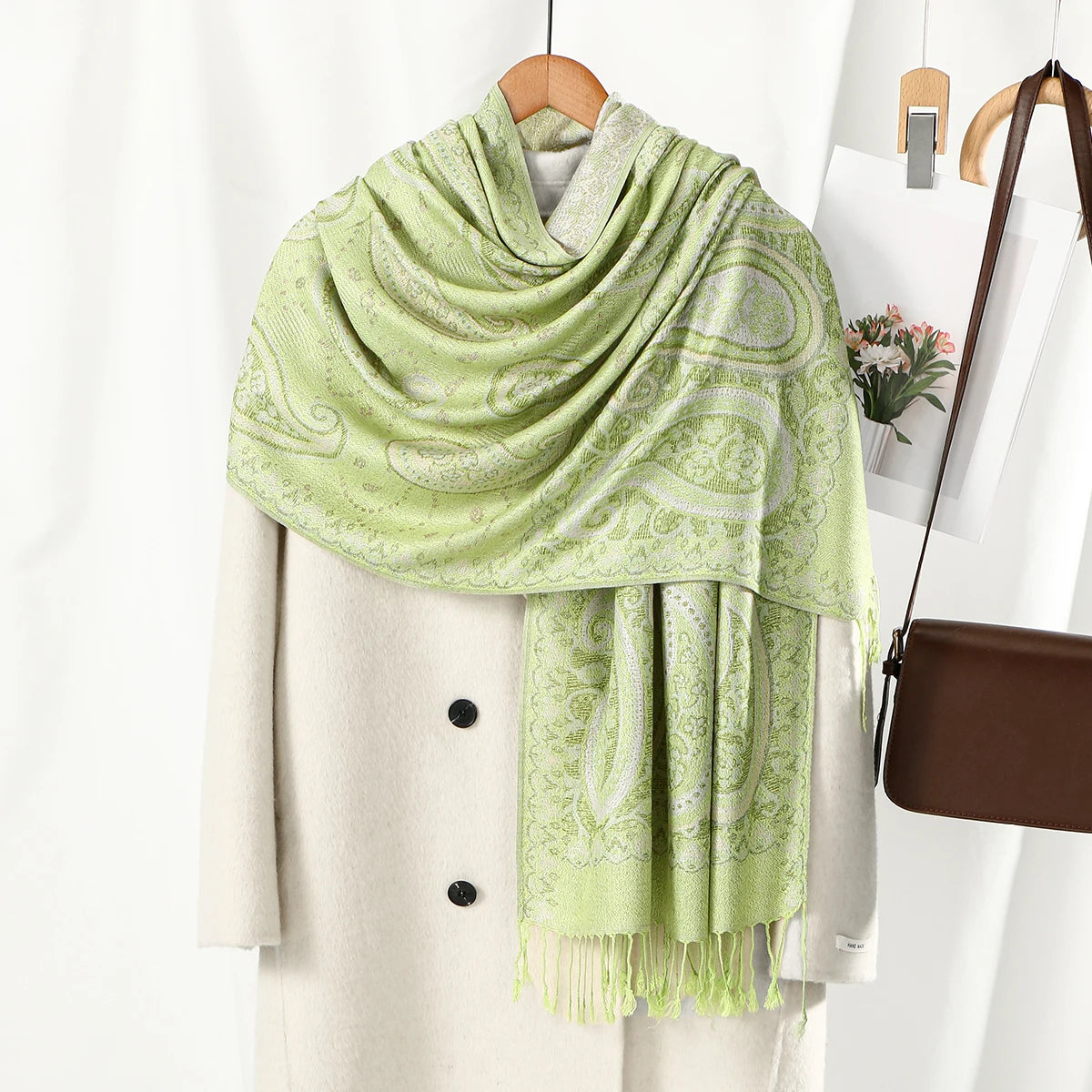 Un chal de bordado paisley vintage verde claro colgado sobre un percha beige.