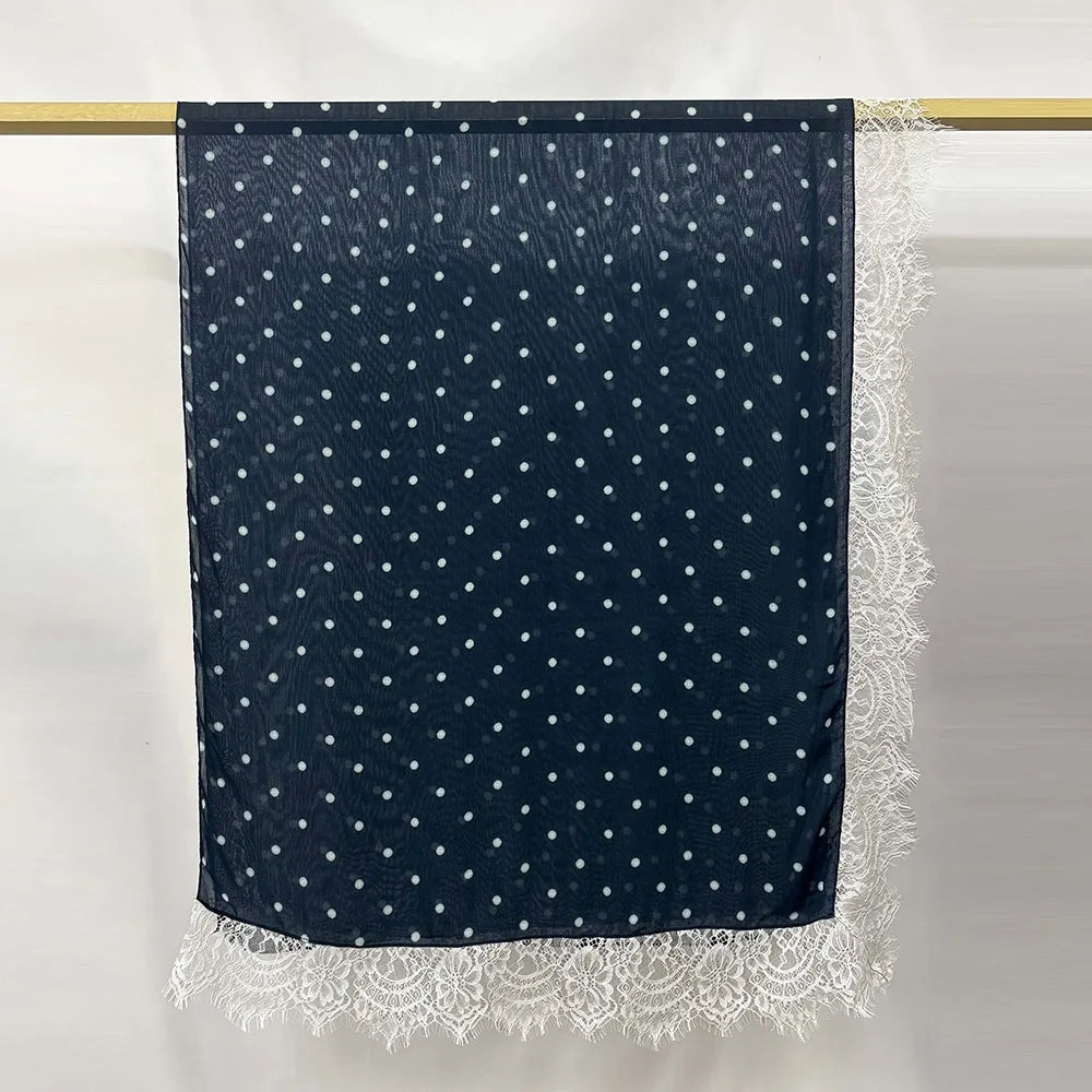 Hijab modal azul marino con lunares blancos y ribete de encaje colgado en una barra.