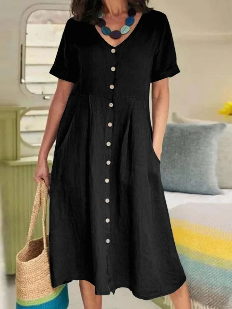 Eine Frau trägt ein elegantes schwarzes Baumwoll- und Hanf-V-Ausschnittkleid mit Knöpfen, steht drinnen.