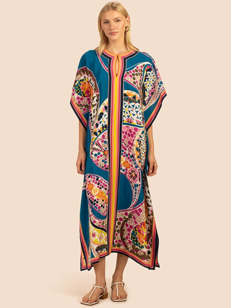 Una modelo viste un vibrante caftán de playa azul con estampados bohemios y bordados coloridos.