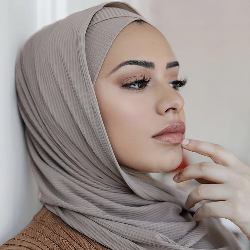 A woman wearing a ribbed jersey hijab scarf in a muted taupe color, shown in profile.