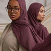 Une femme portant un foulard modal de couleur rose poudré et un haut beige, regardant directement l'appareil photo.