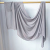 Foulard modal gris uni drapé suspendu sur un bâton en bois contre un mur blanc.