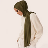 A woman wearing a olive green soft modal jersey hijab scarf and a white sweater.