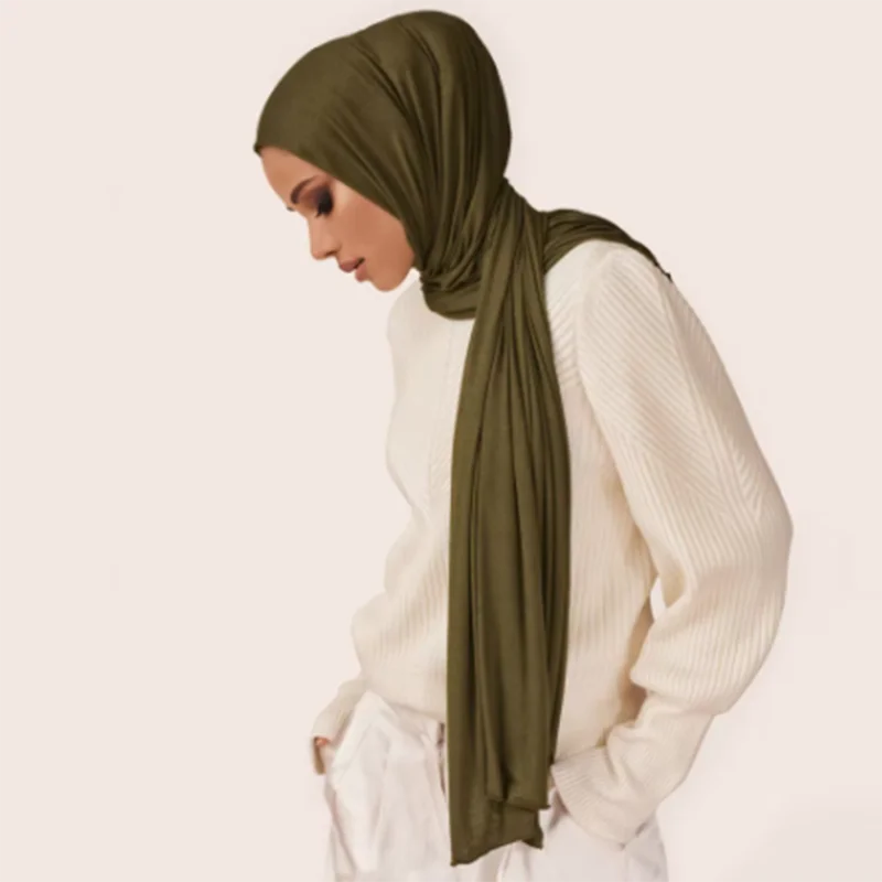 A woman wearing a olive green soft modal jersey hijab scarf and a white sweater.