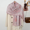Chal de bordado paisley rosa y coral sobre un abrigo beige, con percha a juego visible.