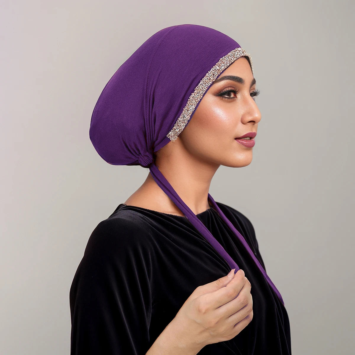 Eine Frau mit lila Diamant-Hijabkappe und schwarzem Samt-Oberteil, im Profil.