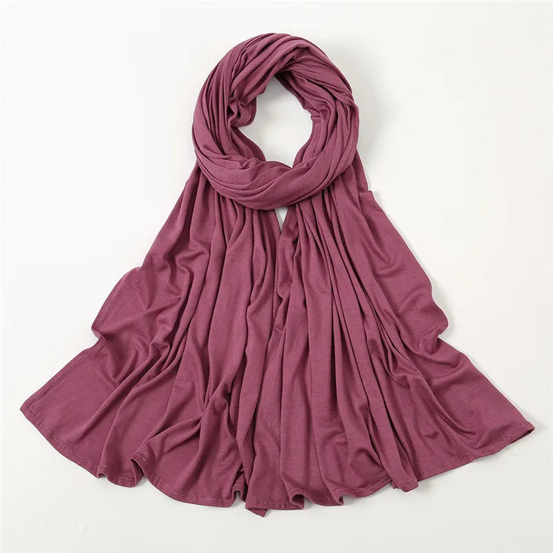 Ein durcherztes Mauve-Jersey-Schal, drapiert und gefaltet auf weißem Hintergrund.