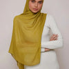 Une femme portant un foulard modal jaune moutarde et une robe blanche.