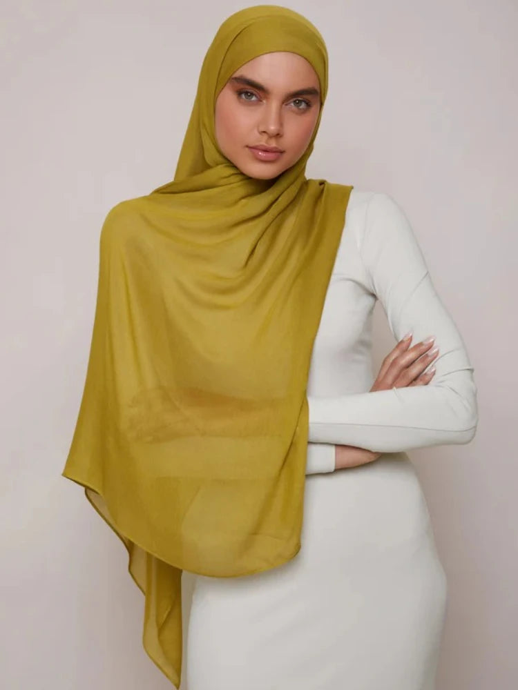 Une femme portant un foulard modal jaune moutarde et une robe blanche.