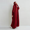Eine Frau in einem maroonen, modesto Abaya mit gerafften Ärmeln vor einer weißen Wand.