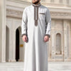 A man wearing a light gray Moroccan ethnic thobe with a stand collar and decorative embroidery.