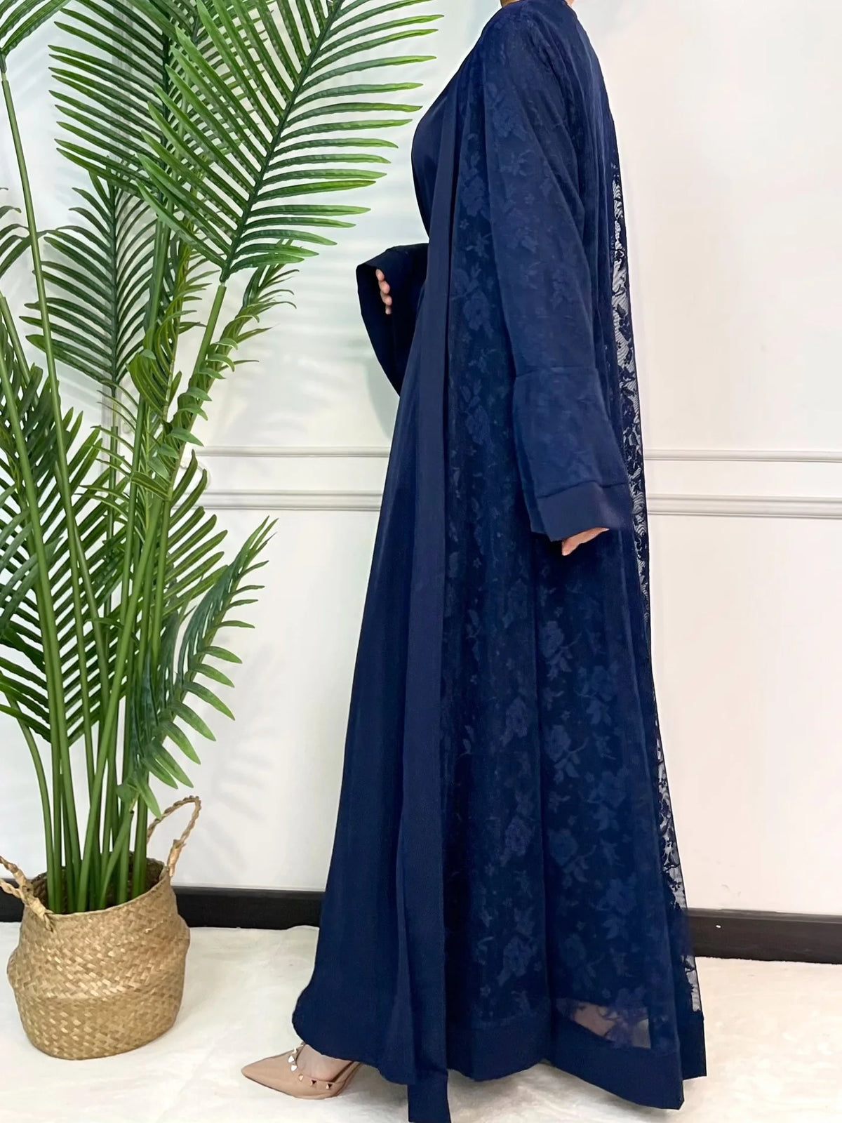 Un ensemble abaya en dentelle bleu foncé pour femmes, exposé à côté d'une grande plante verte.