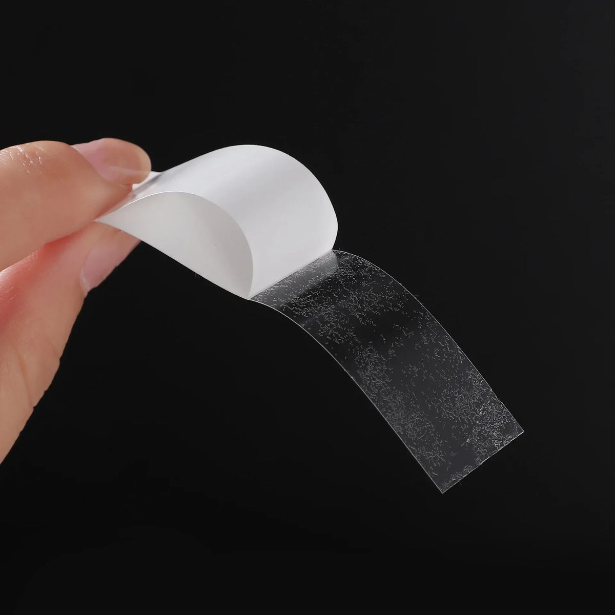 Una mano está quitando un trozo de cinta de hijab transparente y texturizada de un soporte de papel blanco.