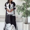 Una mujer modela un cárdigan abrigo abaya plisado de color blanco y negro en un estudio.