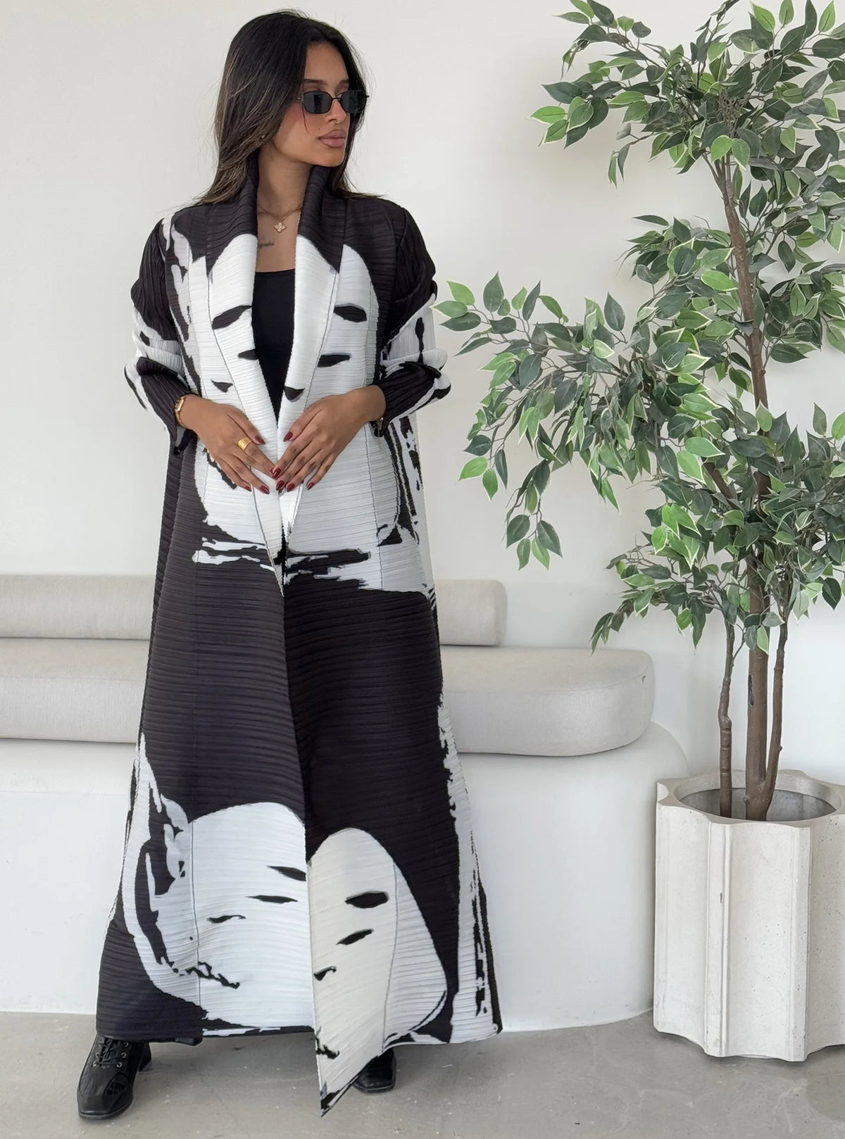 Una mujer modela un cárdigan abrigo abaya plisado de color blanco y negro en un estudio.