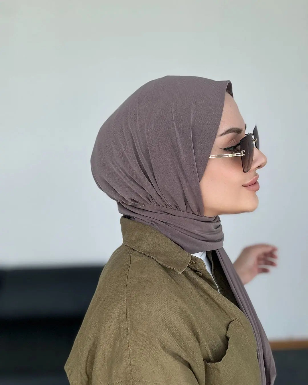Una mujer vistiendo un hiyab instantáneo color malva polvoriento y gafas de sol, mirando hacia un lado.