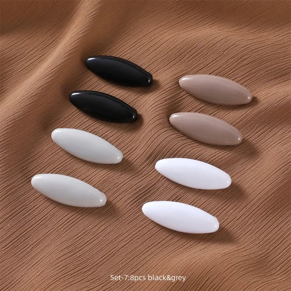 Set of 8 black and grey solid color brooch pins arranged on a brown fabric background