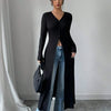 Eine Frau modelliert einen schwarzen, gerippten Strick-Maxi-Cardigan über blauen Jeans in einem Studio.