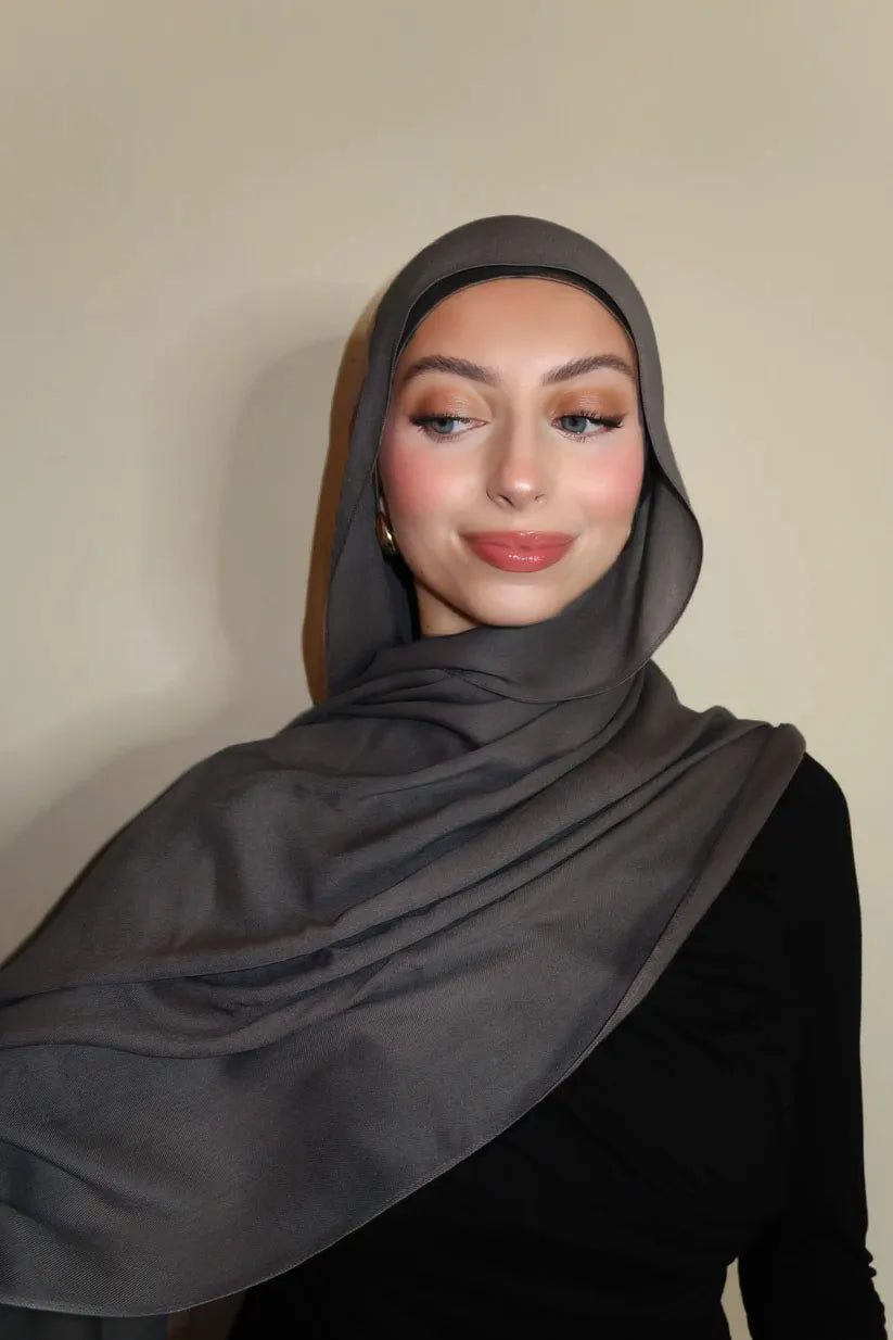 Eine Frau trägt einen einfarbigen grauen Gradient-Rayon-Modal-Hijab und schwarze Kleidung.