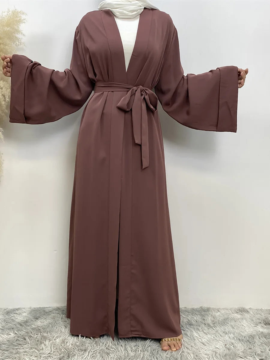 Eine Frau trägt eine fließende, offene Abaya-Kaftan in staubrosa mit einem Gürteldetail.