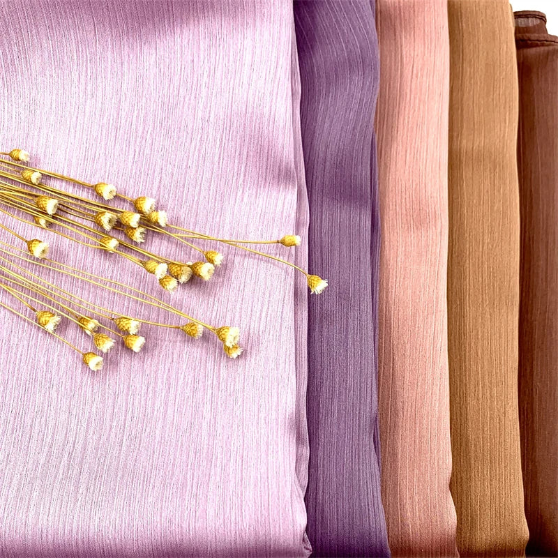Nahaufnahme von Crinkle-Satin-Chiffon-Hijabstoff in verschiedenen Violett-, Rosa- und Beige-Tönen.