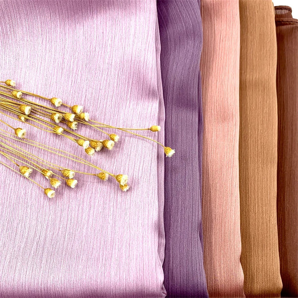 A close-up of crinkle satin chiffon hijab fabric in various shades of purple, pink, and beige.