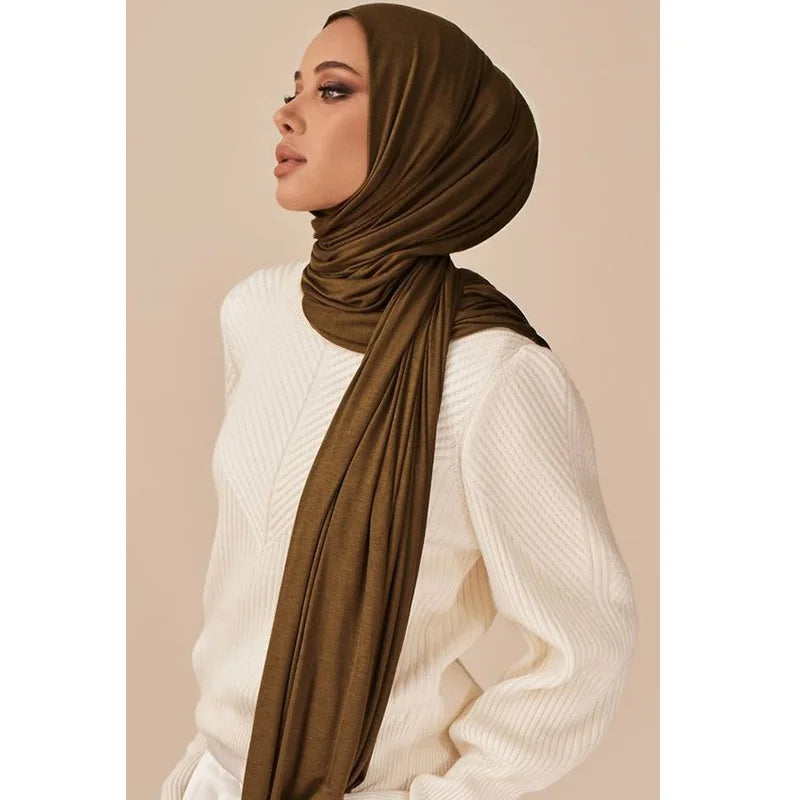 Una mujer vistiendo un pañuelo hijab de algodón modal marrón con una blusa de punto blanca.