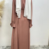 Eine Frau trägt ein fließendes, offenes Abaya Kaftan in staubigem Rosa mit weißem Drappierung.