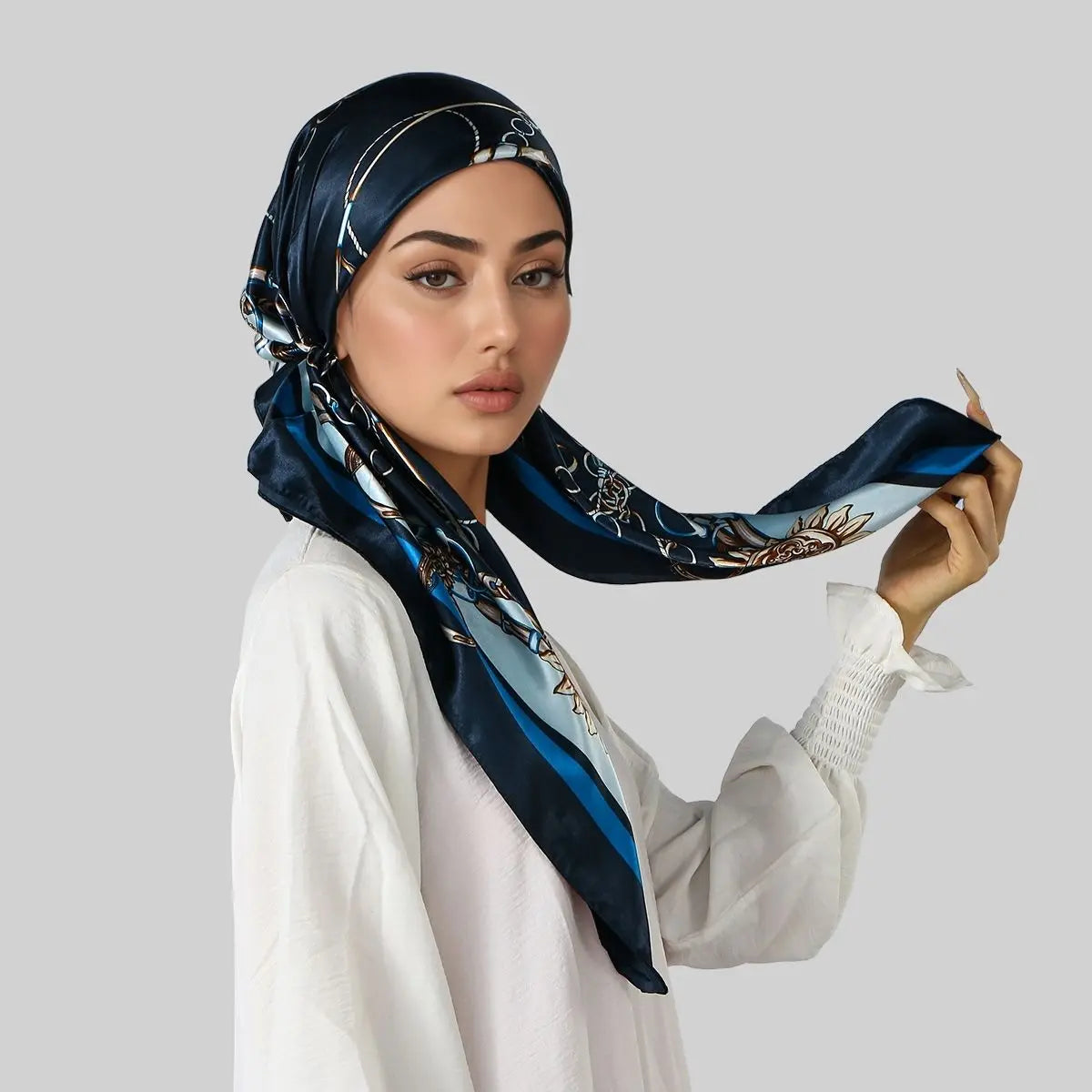 Una mujer vistiendo un turbante hijab de satén azul oscuro con bordado dorado y una blusa blanca.
