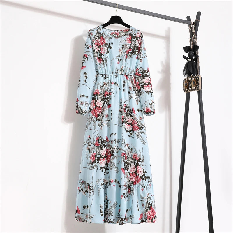 Helles blaues Maxi-Kleid mit Blumenmuster in rosa und grün, an einem schwarzen Haken hängt.