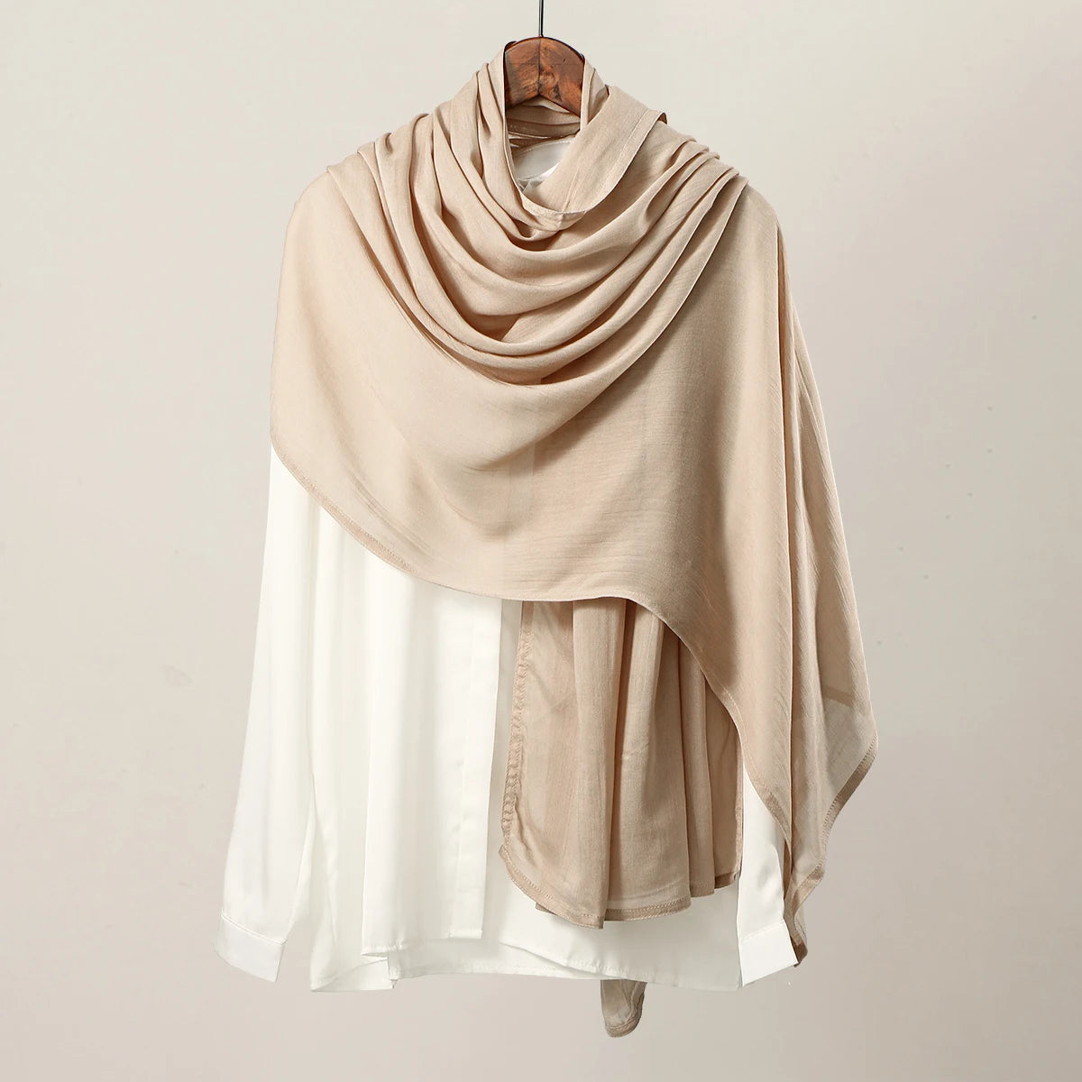 Bufanda de hijab de modal rayón beige drapeada sobre una blusa blanca, exhibida en percha.