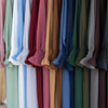 Exhibición de varias abayas de corte holgado en una gama de colores apagados y profundos colgadas en un perchero.