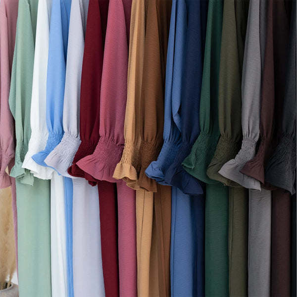 A display of various loose-fit abaya dresses in a range of muted and deep colors hanging on a rack.