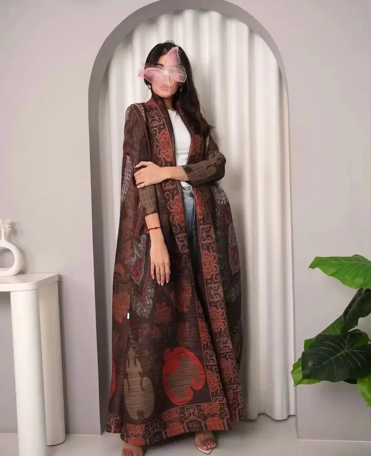 Une femme modélise un trench-coat à plis brun foncé imprimé avec des fleurs et de longues manches sur fond gris clair