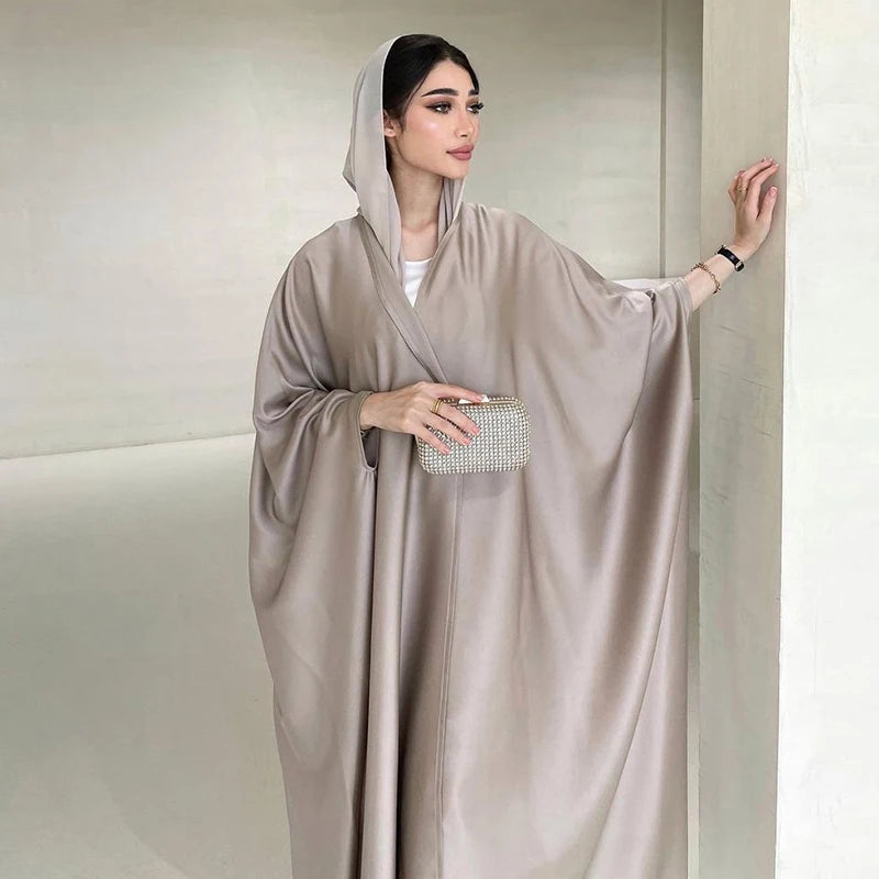 Una mujer vistiendo una abaya de satén beige fluida con capucha y mangas de murciélago.
