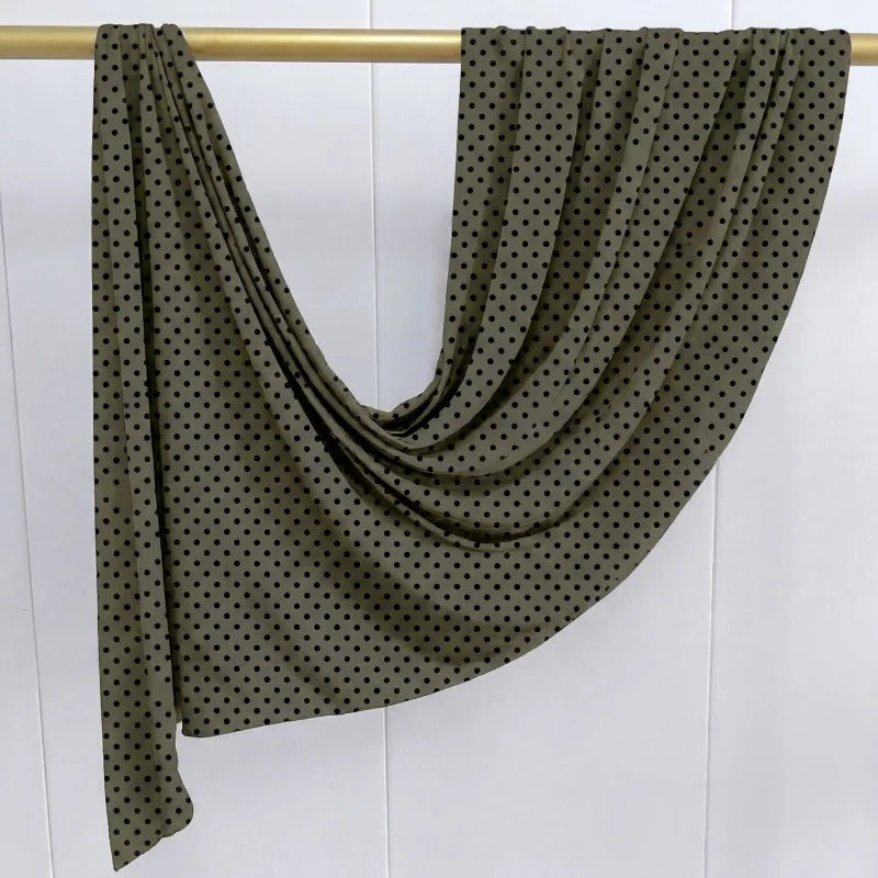 Dunkelolivgrüner Jersey-Hijabschal mit kleinen schwarzen Polka Dots auf einem Holzständer.