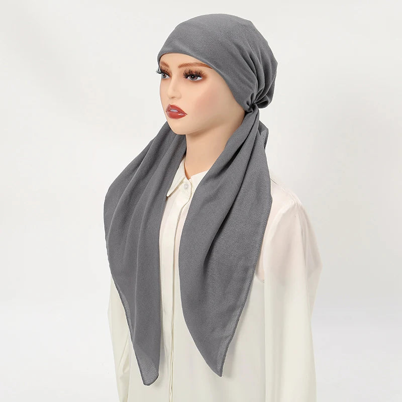 Une femme modélise un bonnet de hijab en lin gris uni drapé autour de son cou, portant un haut blanc.