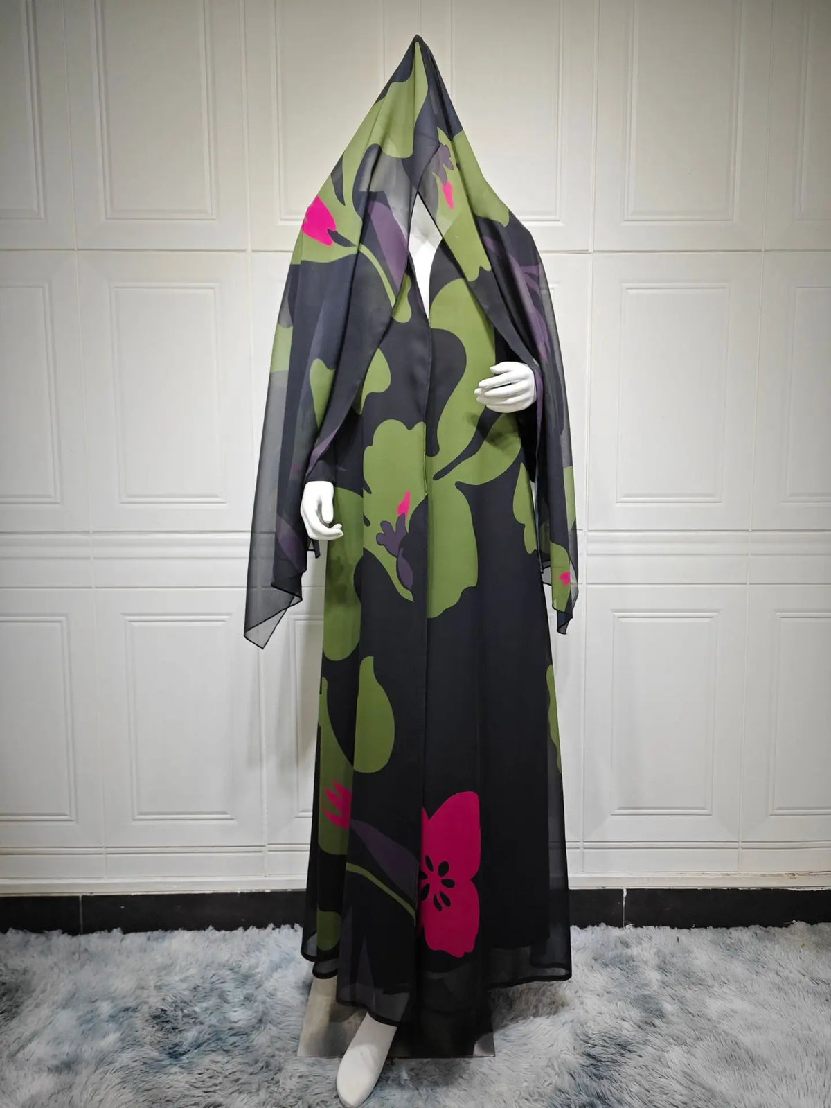 Un conjunto abaya de gasa negra con estampado floral verde y toques rosa, exhibido en maniquí.
