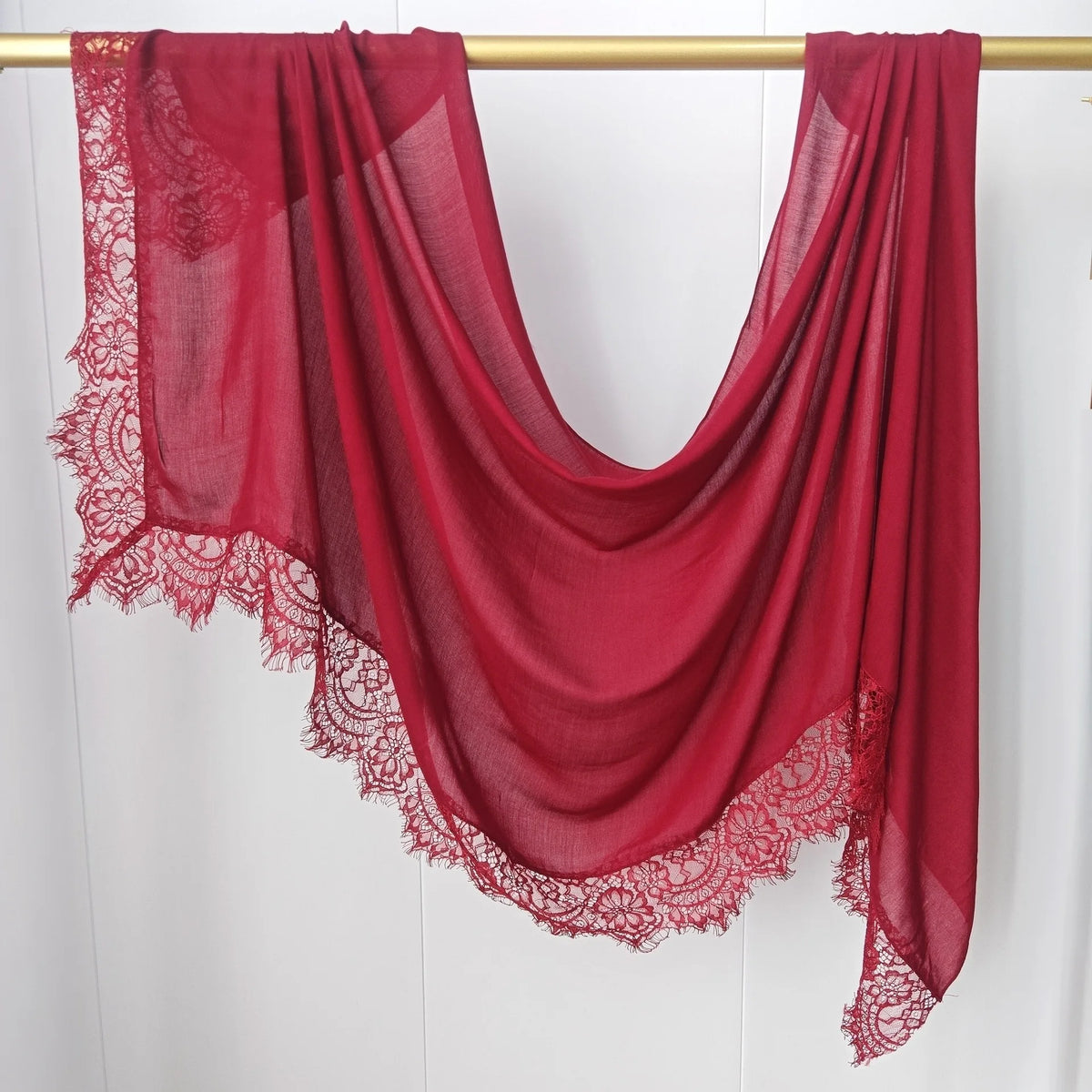 Hijab de encaje rojo intenso drapeado sobre un perchero contra fondo blanco.