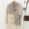 Un abrigo beige junto a una bufanda de bordado paisley vintage con tonos tierra apagados.