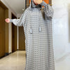 Una mujer vistiendo una abaya de algodón gris con puntos, con capucha, de pie en interiores.
