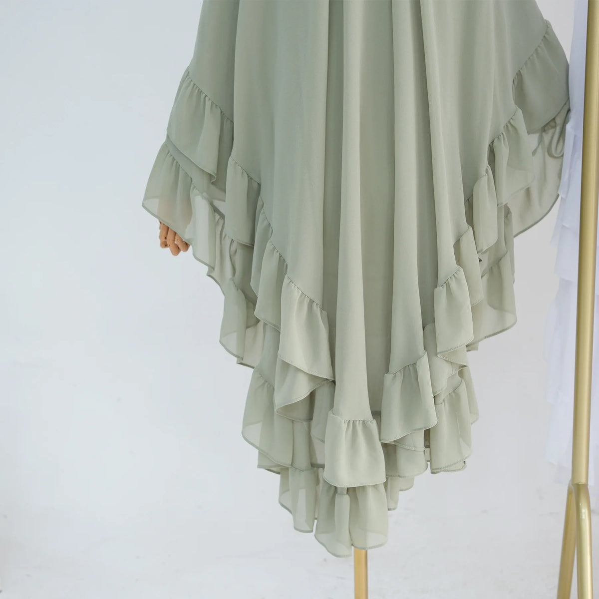 A flowing, light sage green chiffon hijab featuring ruffled layers and a draped design.