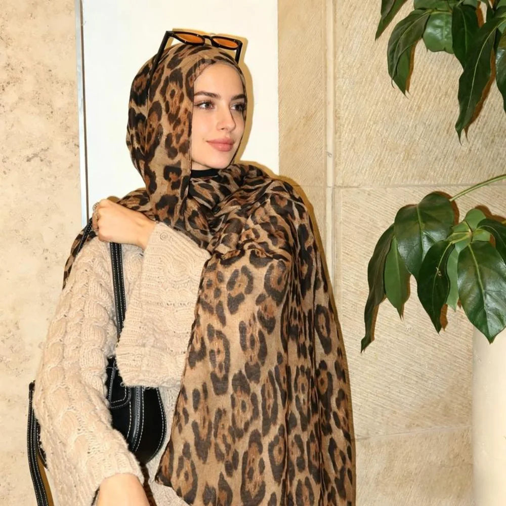 Eine Frau mit Leopardenmuster-Schal und Sonnenbrille steht in einem hellen Innenraum.