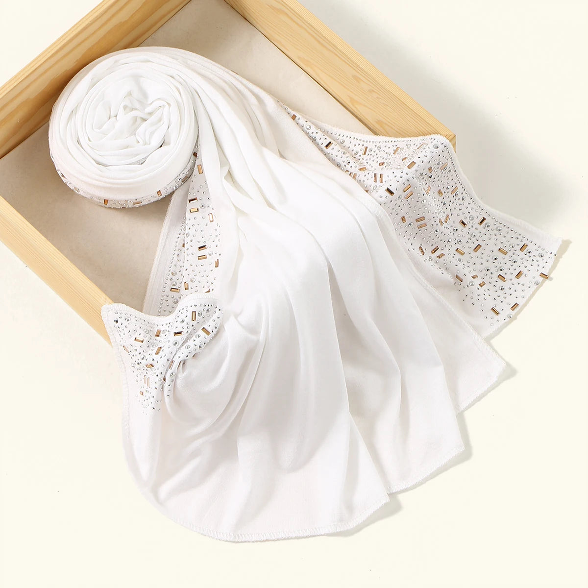 Weißer Luxus-Rhinestone-Hijab-Schal, gerollt und drapiert auf einem Holzrahmen.