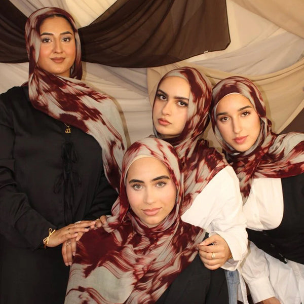 Four women wearing modest hijabs with a watercolour floral print scarf in shades of maroon and white.