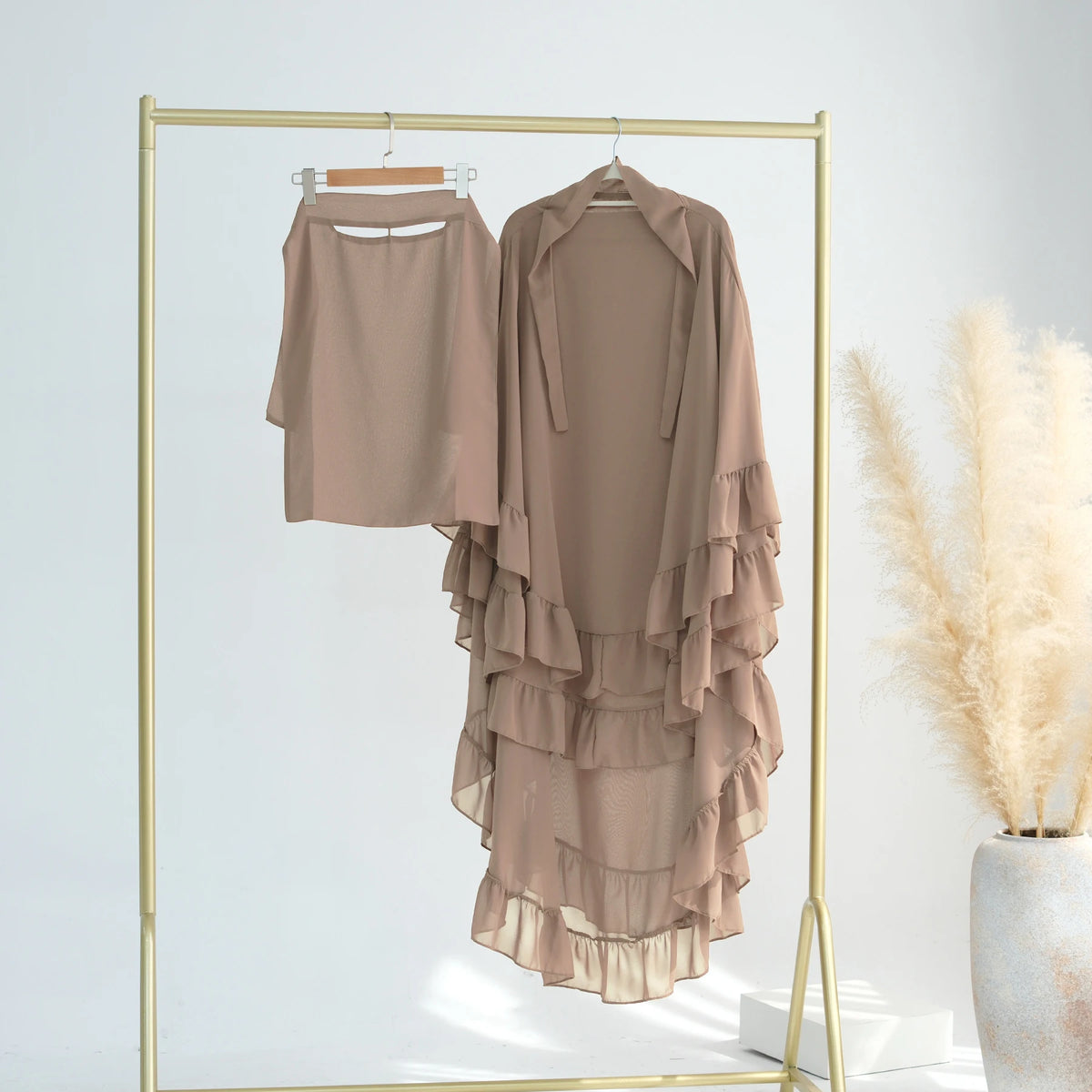 A beige ruffled two-layer chiffon hijab displayed on a gold hanger against a white background.